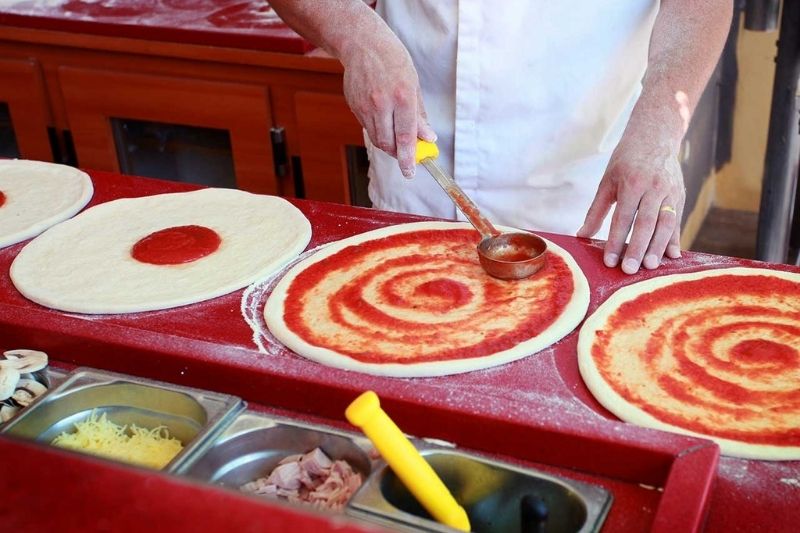 Main étalant de la sauce tomate sur des pizzas avec louche.